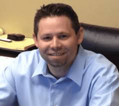 Mike Swerlyk in a blue shirt sitting at a desk.
