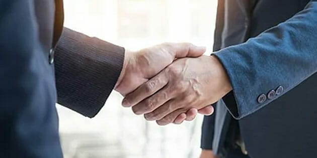 Two businessmen shaking hands in front of a background.